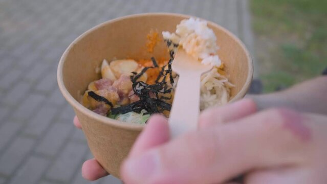 Man eating tuna poke bowl or lunch box in eco paper package. Takeaway food or food delivery and takeout concept. Zero waste lifestyle. Close up