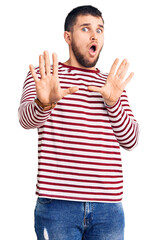 Young handsome man wearing striped sweater moving away hands palms showing refusal and denial with afraid and disgusting expression. stop and forbidden.