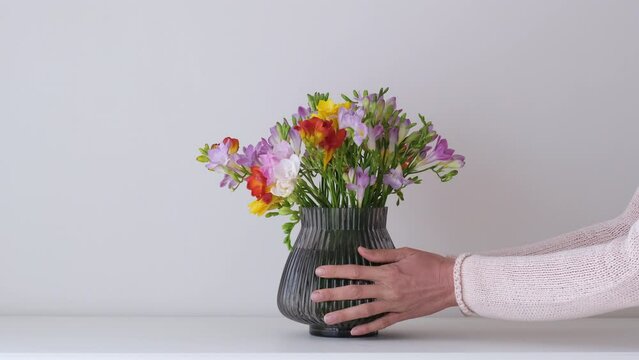 Woman putting a vase with cute colorful flowers on the table