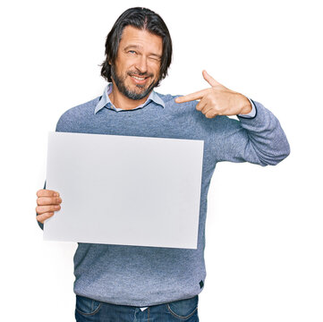Middle age handsome man holding blank empty banner pointing finger to one self smiling happy and proud
