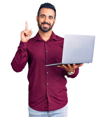 Young hispanic man holding laptop surprised with an idea or question pointing finger with happy...