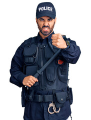 Young hispanic man wearing police uniform holding baton annoyed and frustrated shouting with anger, yelling crazy with anger and hand raised