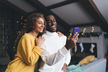 Cheerful interracial couple sharing laugh over social media content; woman in yellow sweater...