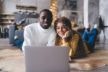 Smiling couple enjoys time on their laptop in a new home, a moment of shared joy in a spacious,...
