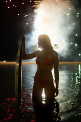 a girl standing with a surfboard in front of fireworks in the ocean in hawaii