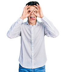 Naklejka premium Young hispanic business man wearing business clothes doing ok gesture like binoculars sticking tongue out, eyes looking through fingers. crazy expression.