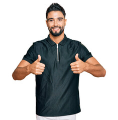 Young man with beard wearing sportswear success sign doing positive gesture with hand, thumbs up smiling and happy. cheerful expression and winner gesture.