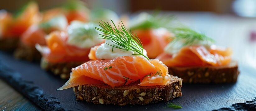 Salmon canapes with cheese cream, dill, on brown bread, served on a black slate platter.