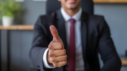 Confident businessman in a suit gives a thumbs up in a modern office setting, signaling success or agreement