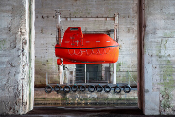 Red lifeboat suspended from a crane in a harbour