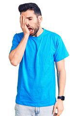 Young handsome man with beard wearing casual t-shirt yawning tired covering half face, eye and mouth with hand. face hurts in pain.
