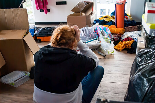 Tired woman sits on the floor and holds her head at the sight of the upcoming work. Moving to a new apartment. Packing things in boxes