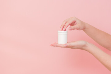 Hand with blank white plastic tube on pink background. Cosmetics beauty mockup for product branding