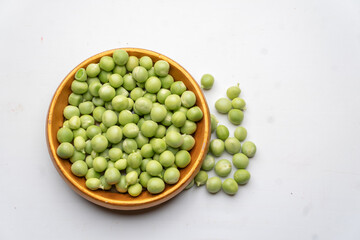Top view of a brown saucer of green peas, fresh peas on a white background