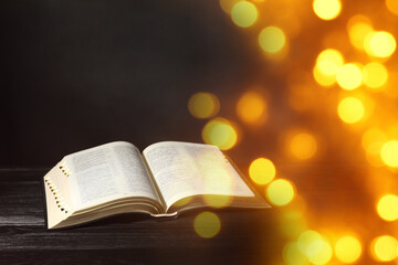 Open Bible on black wooden table, bokeh effect