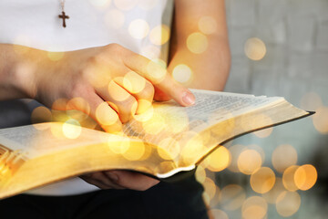 Woman reading Bible near white wall, closeup. Bokeh effect