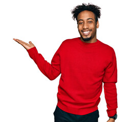 Young african american man with beard wearing casual winter sweater smiling cheerful presenting and...