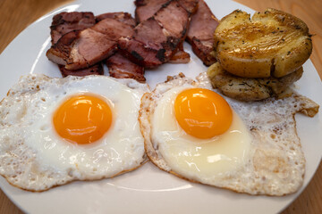 Two fried eggs with gammon and potato patties on a white plate. - 710130128