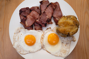 Two fried eggs with gammon and potato patties on a white plate. - 710130140