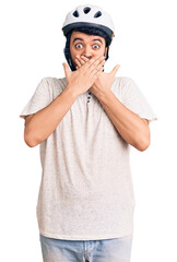 Young hispanic man wearing bike helmet shocked covering mouth with hands for mistake. secret concept.