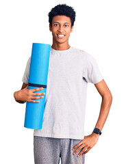 Young african american man holding yoga mat looking positive and happy standing and smiling with a...