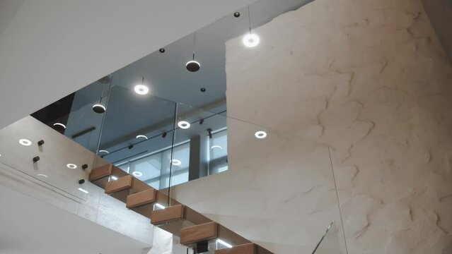 Chandeliers and many rounded lamps hangs from the ceiling near the stairs indoor. Hanging lamps over stairs in two-story apartment, lamps turned on, slow motion dolly shot.