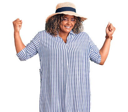 Young african american plus size woman wearing summer hat showing arms muscles smiling proud. fitness concept.