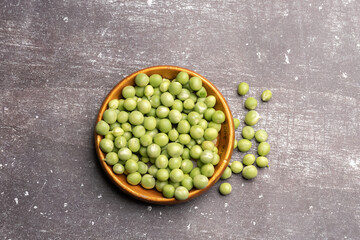 Top view of a brown saucer of green peas, fresh peas on a dark gray background.