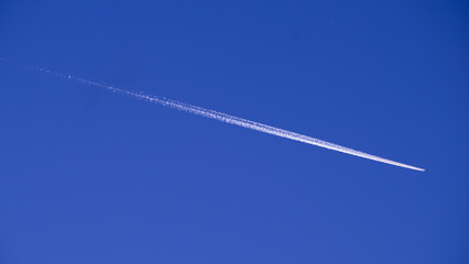 flying airplane in the cobalt blue sky, white plane trail on blue background