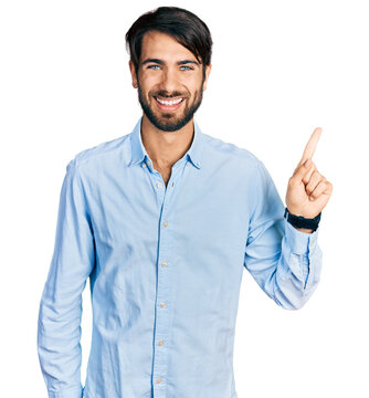 Hispanic man with blue eyes wearing business shirt with a big smile on face, pointing with hand finger to the side looking at the camera.
