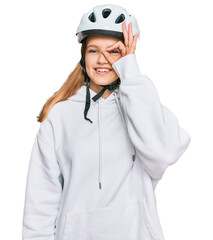 Beautiful young caucasian girl wearing bike helmet smiling happy doing ok sign with hand on eye looking through fingers