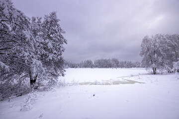 Winter landscape with a river covered in snow, fishermen in the background