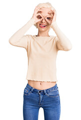 Young blonde woman wearing casual clothes doing ok gesture like binoculars sticking tongue out, eyes looking through fingers. crazy expression.