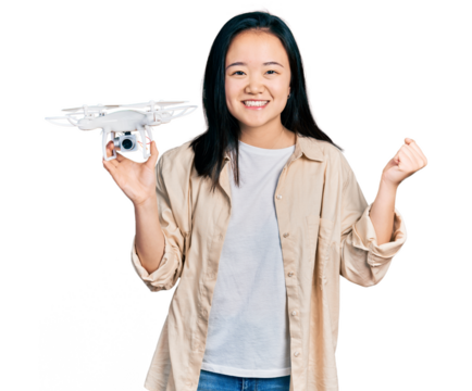 Young chinese woman holding drone screaming proud, celebrating victory and success very excited with raised arm