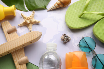 Composition with bottles of sunscreen cream, world map, wooden plane, starfish and flip-flops on green background