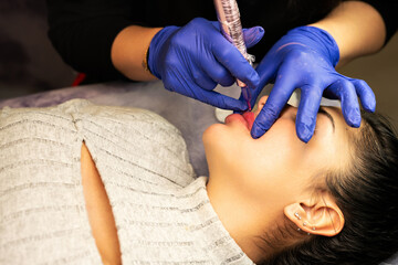 Young woman having permanent makeup on lips in beautician salon. Close up