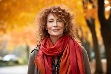 A radiant mature woman with auburn curls, donning an elegant scarf, exuding confidence and grace as she strolls through a vibrant autumn park - obrazy, fototapety, plakaty