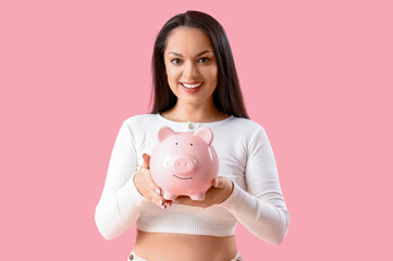 Fototapeta na wymiar Young woman with piggy bank on pink background