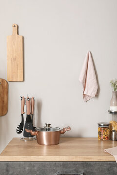 Wooden kitchen counter with cooking pot, utensils and cutting board hanging on white wall