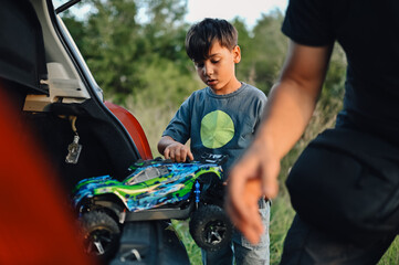 Boy is taking his toy race car out of open car trunk before driving it outside