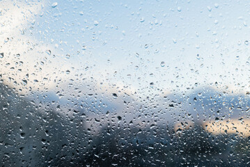 Raindrops on glass in cloudy weather and a blurry image of the city. Background in gray-blue tones.