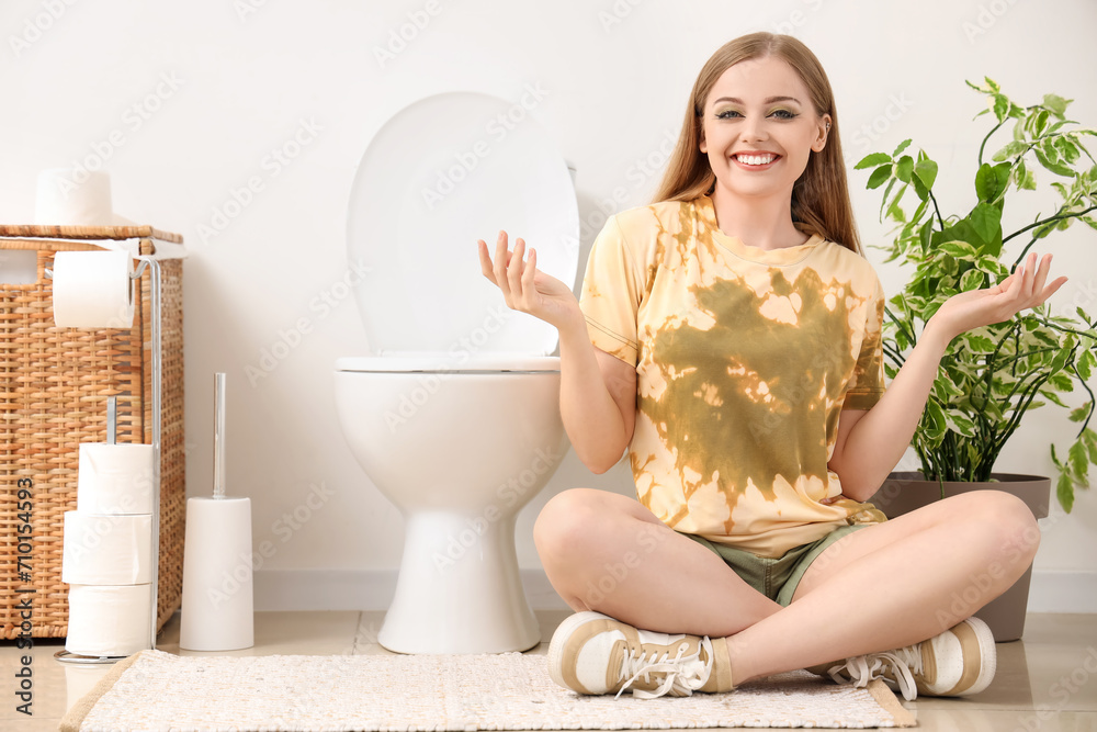 Wall mural Young woman sitting near toilet bowl in restroom