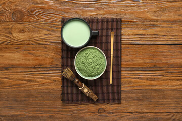 Cup of fresh matcha tea, powder and accessories on wooden background
