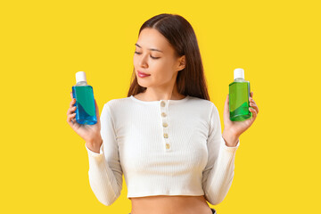 Young Asian woman with mouth rinse on yellow background