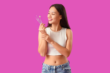 Smiling young Asian woman with dental tools on purple background - obrazy, fototapety, plakaty