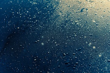 Close-up of water droplets on a dark blue surface with highlights and reflections, creating a fresh and clean feeling.