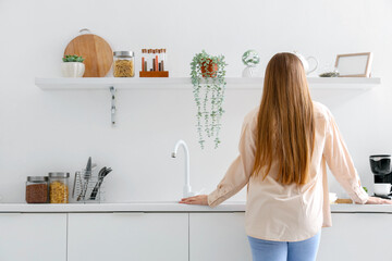 Back view of young woman standing near white counters in modern kitchen