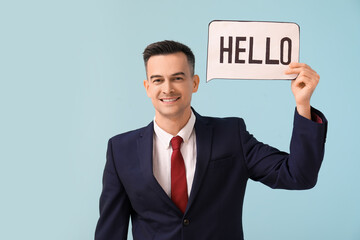 Handsome businessman holding paper with word HELLO on blue background