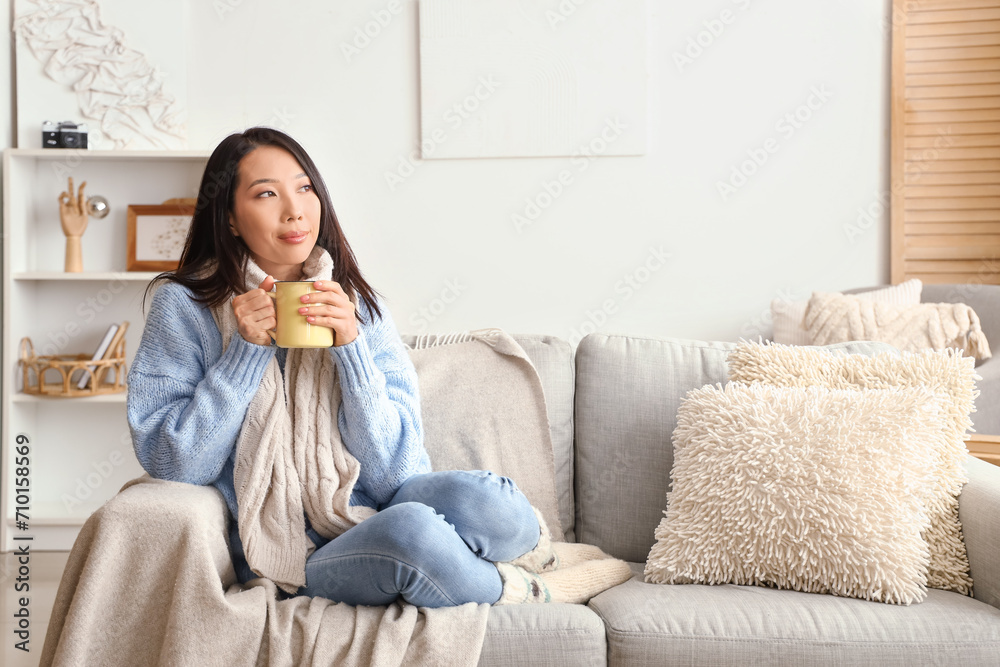 Wall mural young asian woman with cup of hot tea sitting on sofa at home