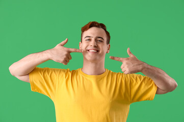 Fototapeta premium Young man pointing at his teeth on green background, closeup